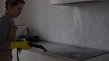 Ev temizliği. Kız buharlı temizleme fırçası mutfak beyaz elektronik kıssa buharı eldivenlerde. Yüzeyin temizlenmesi. hafif mutfak