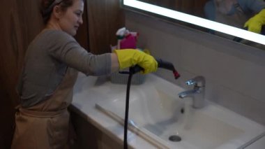 Kadın evde banyo temizliği yapıyor, kadın fayans duvarını buharla yıkıyor. Hızlı temizlik için buhar temizleyicisi kullanılıyor..