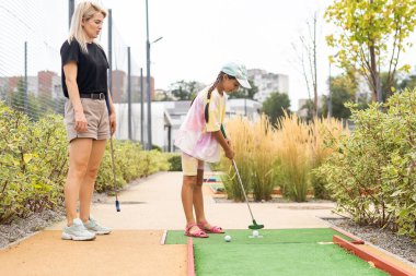 mother and daughter playing mini golf, children enjoying summer vacation.