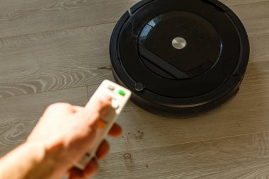 Cep telefonu ve modern uzaktan kumandalı robot elektrikli süpürgesi olan bir kadın.