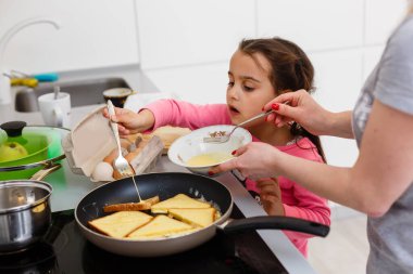 Küçük kız annesiyle mutfakta yemek pişiriyor.