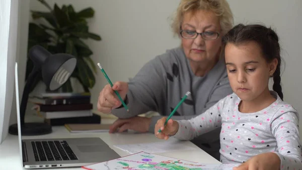 소녀는 할머니와 집에서 공부하고 노트북을 교육용으로 사용하고 온라인 공부를 집에서 — 스톡 사진