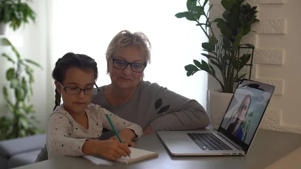 소녀는 할머니와 집에서 공부하고 노트북을 교육용으로 사용하고 온라인 공부를 집에서 — 스톡 사진