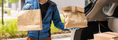 Kargo aracının önünde koruyucu maske takan postacı Coronavirus hastalığı veya COVID-19 nedeniyle paket teslim ediyor..