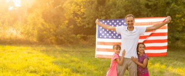 Amerikan bayrağı taşıyan ebeveynler ve çocuklar renkli bir uçurtmayla oynuyorlar. Anne, baba ve küçük kızları sisli bir günde 4 Temmuz 'u birlikte kutluyorlar. ABD 'nin Bağımsızlık Günü konsepti