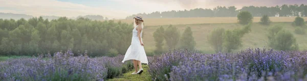 Beautiful young woman in wicker hat and white dress in a lavender field with.