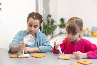 İki güzel kız kardeş, ahşap bir masada lezzetli pastalar süsleyip yiyorlar..