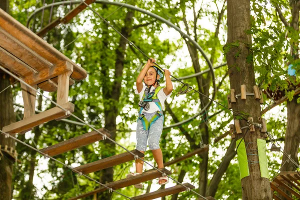 小女孩站在绳子上 双手拿着绳子 在缆绳公园里的小孩通过障碍物 — 图库照片