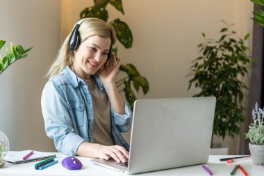 İnternette toplantı. Kulaklık takan genç bir kadın dizüstü bilgisayar kullanarak webinar izliyor ya da web kamerasıyla görüntülü konuşma yapıyor. İş konferansı. E-öğrenim eğitim kavramı.