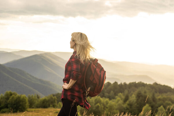 Beautiful young woman with backpack walking on meadow. Portrait of hiker girl outdoor.