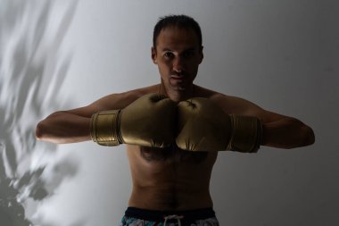 Confident young fit sportsman wearing boxing gloves isolated over white background, boxing.