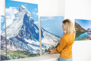 Canvas print with gallery wrap interior decor. Woman hangs landscape photography on white wall. Hands holding photo canvas print.
