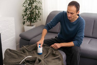 İplikten örgü ören kumaşları temizlemek için kablosuz cihaz. Adam kazaktaki ipliği çıkarıyor.