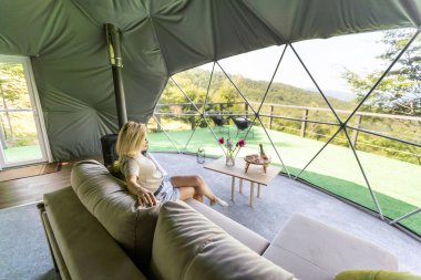 Glamping 'de şeffaf kabarcık çadırı, etrafındaki ve içindeki yemyeşil orman. Kadın glamping dinleniyor.