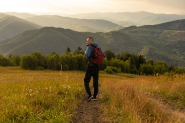Sırt çantalı bir turist sırtında sırt çantasıyla dağlarda duruyor..