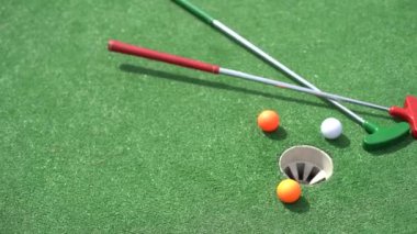 Mini-golf clubs and balls of different colors laid on artificial grass