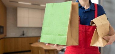 Kağıt cep ve yiyecek kapları gülen bir teslimatçının elinde. - Bir restoranın kaliteli servisi.