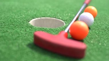 Mini-golf clubs and balls of different colors laid on artificial grass