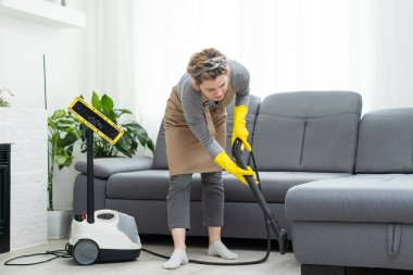 Woman cleaning couch with vacuum cleaner at home. clipart