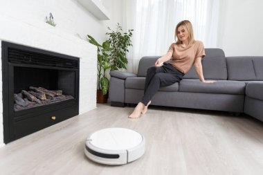 Dinlenen kadının olduğu koltuğun yanındaki modern robot elektrikli süpürge..