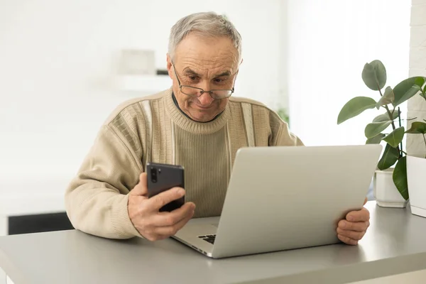 集中高级男人在笔记本电脑和电话在家看 — 图库照片
