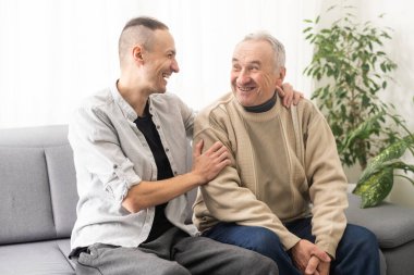 Young adult caucasian son listening and supporting his old elderly senior father at home indoors. Care and love concept