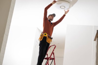 Üniformalı elektrikçi içeride tavan lambasını tamir ediyor..