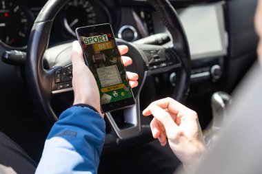 Bahisçilerin web sitesi ekranında cep telefonuyla el ele tutuşan bir adamın yakın plan çekimleri. Erkek kumarbaz, mobil uygulama kullanarak online bahis oynuyor. Arabada beyaz oturuyor.