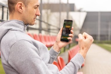 Yakışıklı, gülümseyen sakallı bir adamın portresi bahisçilerin mobil uygulamasını kazanmaktan mutlu oluyor. En sevdiği futbol takımına, arka plandaki stadyuma bahis oynadıktan sonra..