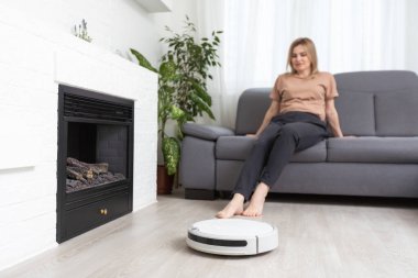 Dinlenen kadının olduğu koltuğun yanındaki modern robot elektrikli süpürge.