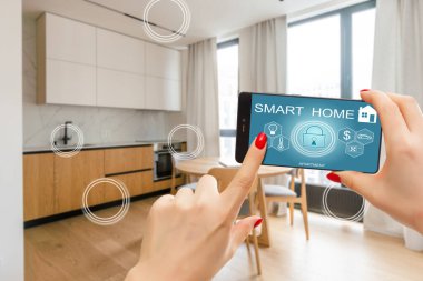 Akıllı ev arayüzü çift pozlama ile bulanık mutfakta akıllı telefon tutan kadın eli. Otomasyon kavramı
