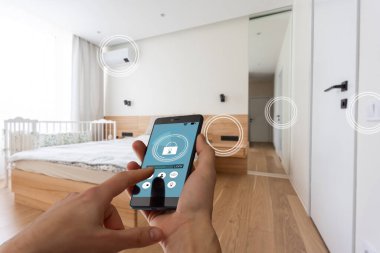 Akıllı ev otomasyon uygulaması arka planda ev içi olan kadın eliyle akıllı telefondan tutulan.