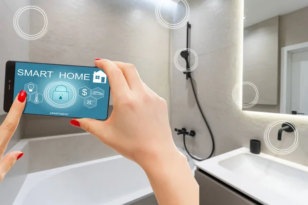 stock image Smart home automation app on smartphone hold by female hand with home interior in background.