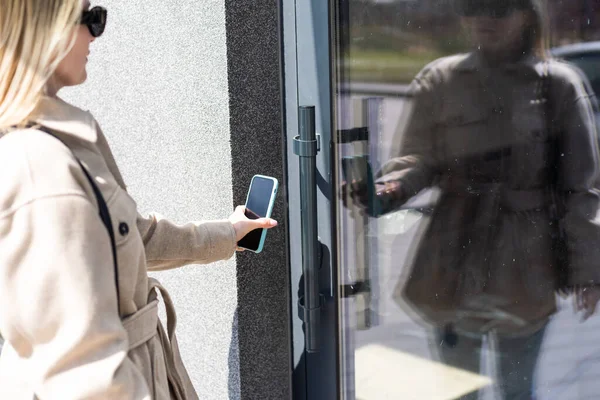 Woman puts the smart phone to the electronic reader to access the apartment or office. Cell with running mobile secure application.