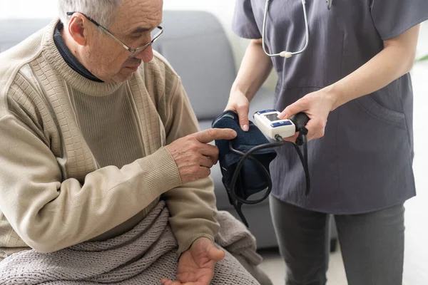 若い女性医師は 病院での会議で成熟した患者の血圧をチェック聴診器で白い制服を身に着けています デジタルクロノメーターを使用して深刻な医師のGp — ストック写真