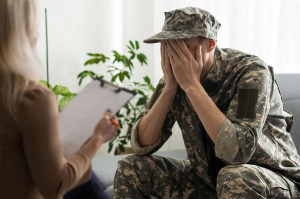 sad soldier with ptsd talking at psychiatrist and gesturing while sitting on couch during therapy session.