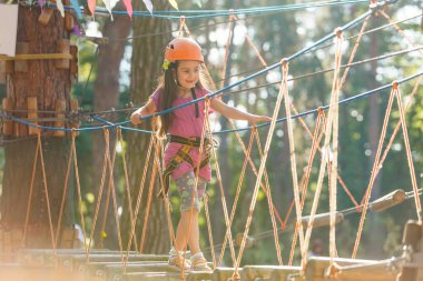 Sıcak ve güneşli bir yaz gününde macera parkına tırmanarak eğlenen sevimli küçük kız. Küçük çocuklar için yaz etkinlikleri. Çocuk okul tatillerinde eğleniyor..