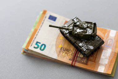 Ahşap arka planda bir yığın avro banknotunda plastik oyuncak tankları.