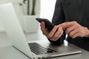 Bilgisayarla çalışan bir iş adamı, elinde akıllı bir telefonla. Bilgisayar masanın üstünde. İş konsepti
