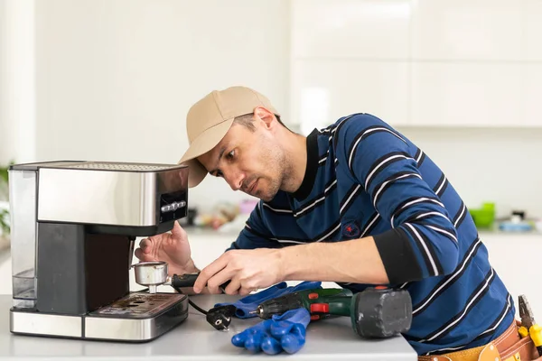 Professional young repairman repairs a coffee maker. Handsome worker in uniform repairing coffee machine in a workshop