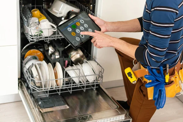 Handyman with tablet pc repairing domestic dishwasher in the kitchen
