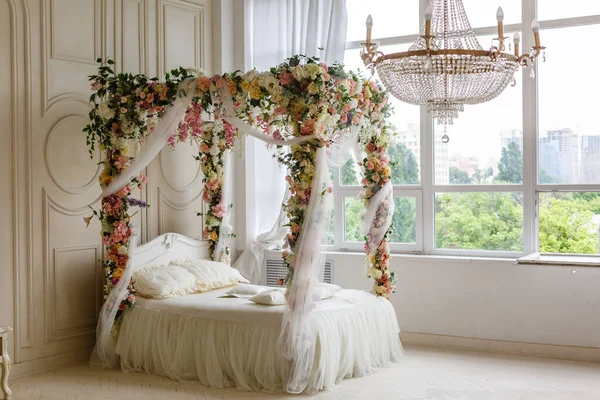 white bed. white bed in a classic style with a garland of leaves and flowers. the spring location. decorated in a spring decor. the white four-poster bed is decorated with flowers