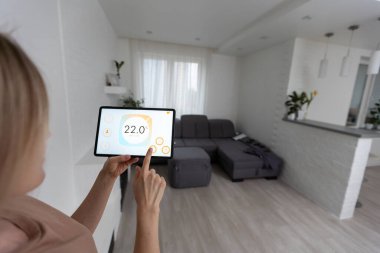 Oturma odasındaki duvara dijital bir dokunmatik ekranla evi kontrol eden kadın..