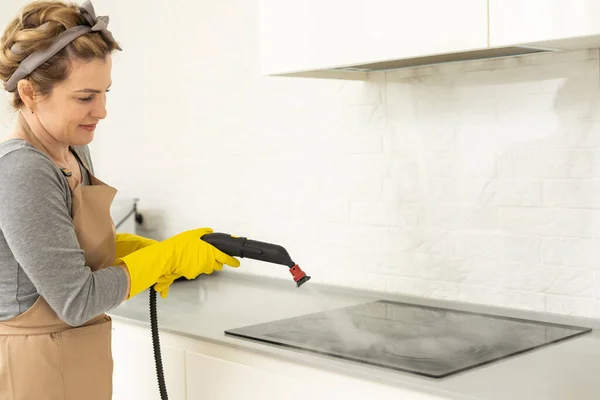 打扫房子女孩拿着一个电动蒸汽清洁器 用湿热的蒸汽清洗厨房的提液和表面 表面的清洁 绿色手套 轻便公寓电炉 — 图库照片