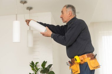 Erkek bir elektrikçi tavan lambasındaki ampulleri değiştirir. Erkeklerin ev işleri. Evde elektrikli aletlerin bakımını üstlenmek..