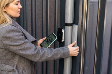 Kadın, cep telefonundaki uygulamayı kullanarak erişimi sağlamak ve binadan geçmek için gizli anahtar kodu giriyor, akıllı ev sistemini etkisiz hale getirmek için kontrol panelindeki düğmelere basıyor.