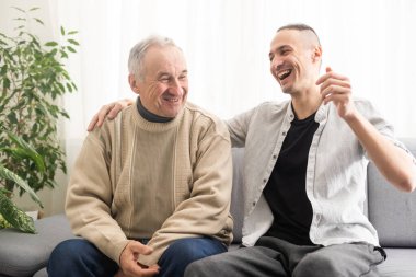 Young adult caucasian son listening and supporting his old elderly senior father at home indoors. Care and love concept