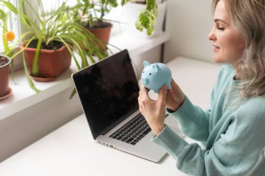 Erken yaşlarda maaş tasarrufu yapmayı planlayan genç bir kadın domuz kumbaralı dizüstü bilgisayar kullanarak para biriktiriyor.