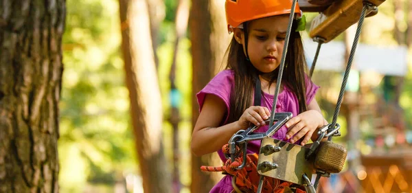 stock image Little brave caucasian girl treerunner fasten the carabiner clip before climbing at outdoor treetop climbing adventure park.