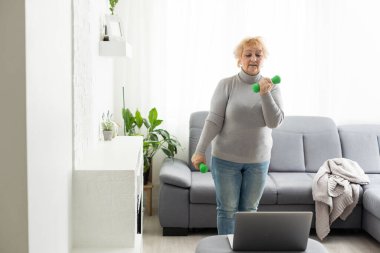 Evde antrenman. Sportif son sınıf öğrencisi laptopta ders izlerken yoga tahtası yapıyor oturma odasında egzersiz yapıyor, boş yer, panorama..